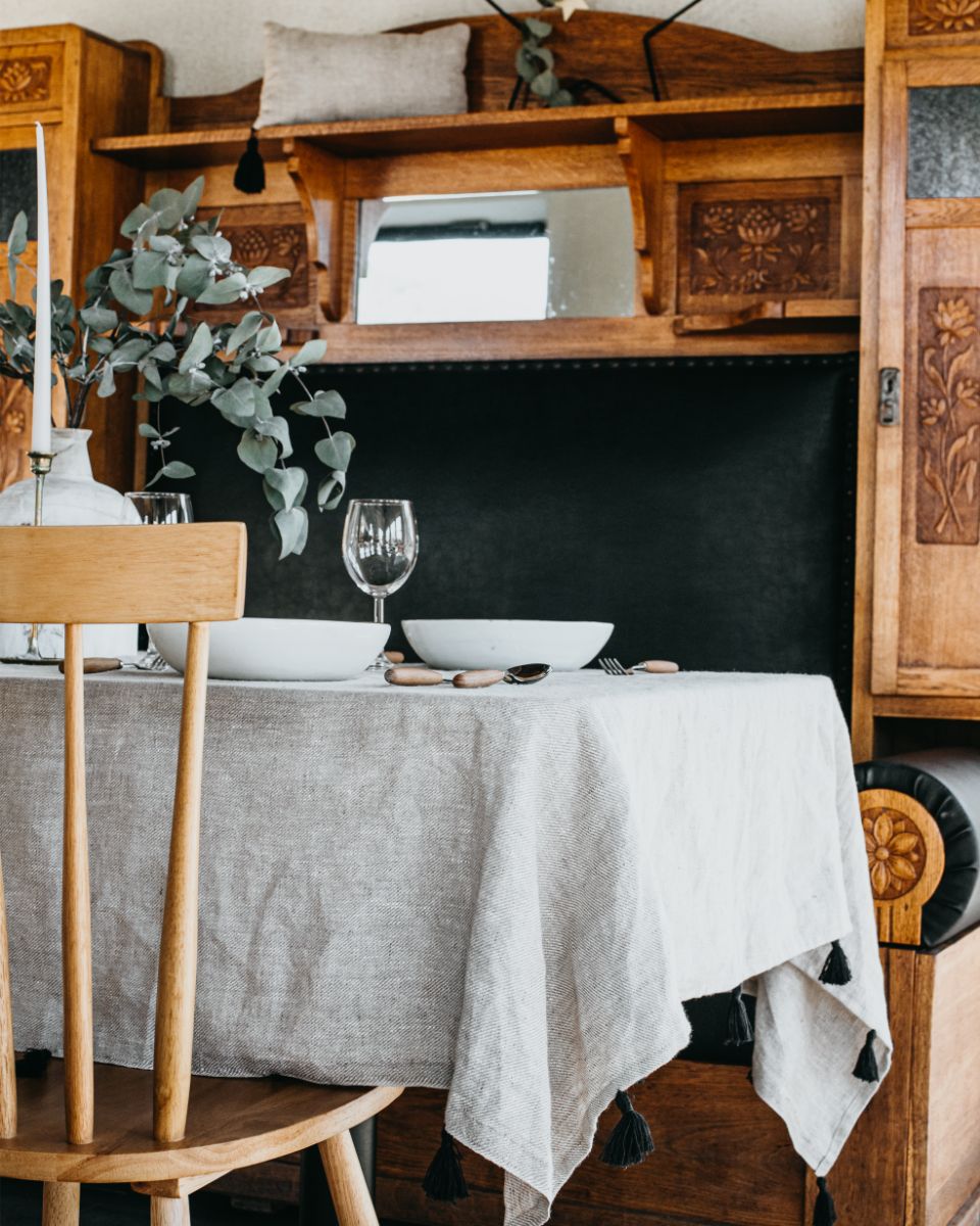 revený jedálenský stôl s hrubým ľanovým obrusom a bielymi taniermi.