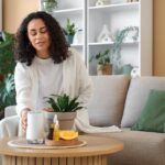 Žena sediaca na sedačke v modernom interiéri nastavuje difuzér na konferenčnom stolíku.