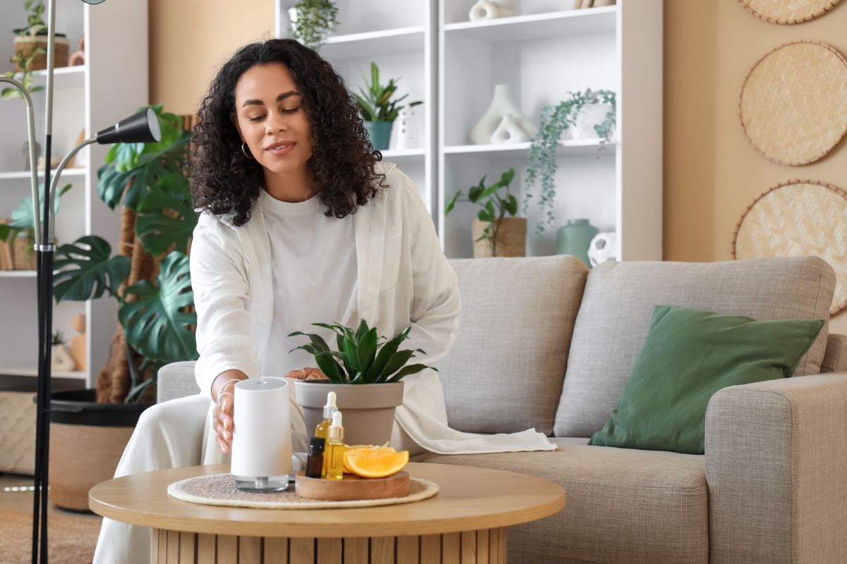 Žena sediaca na sedačke v modernom interiéri nastavuje difuzér na konferenčnom stolíku.