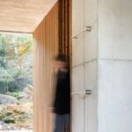 Časť interiéru s betónovou stenou s antikorovými držadlami a ďalšou stenou s dreveným obložením.