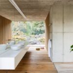 Biele keramické umývadlá na dlhej bielej skrinke v kúpeľni s výhľadom do zelenej záhrady.