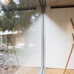 g Drevený maliarsky stojan pri bielej vstavanej skrini a presklenej stene.