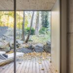 Presklené posuvné dvere s priamym vstupom na drevenú terasu s roztrúseným lístím a bielym ležadlom.