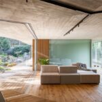 Béžová sedačka na drevenej podlahe pod surovým betónovým stropom v otvorenom interiéri.