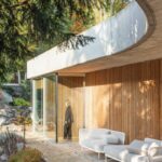 Organicky tvarovaná betónová rímsa nad drevenou fasádou s bielymi exteriérovými pohovkami na terase.