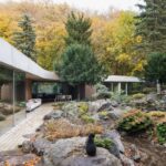 Organicky tvarovaná moderná architektúra s dreveným obkladom pri členitom záhradnom jazierku s balvanmi.