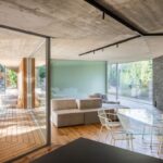 Sklenený jedálenský stôl s bielymi stoličkami a béžová sedačka v interiéri s presklenými fasádami.