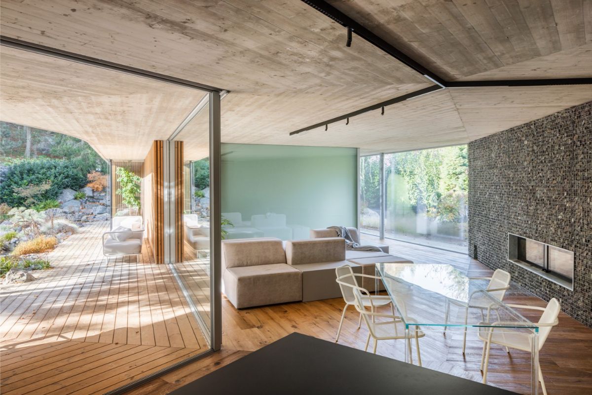 Zelená stena, drevo i surový kameň odrážajú prírodu za presklenými stenami. Dom o to viac splýva s okolitým prostredím.