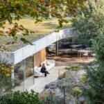 Moderný dom so zelenou vegetačnou strechou a terasou s bielou sedačkou.