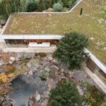 Zelená strecha na modernom dome s drevenou terasou pri jazierku a skalnatej záhrade.