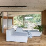 Svetlosivá rohová pohovka na dubových parketách v minimalistickom priestore s dreveným lamelovým obkladom.