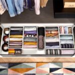 Otvorená biela šatníková zásuvka s priehradkami a farebným textilom.