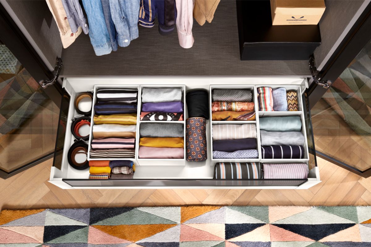 Otvorená biela šatníková zásuvka s priehradkami a farebným textilom.