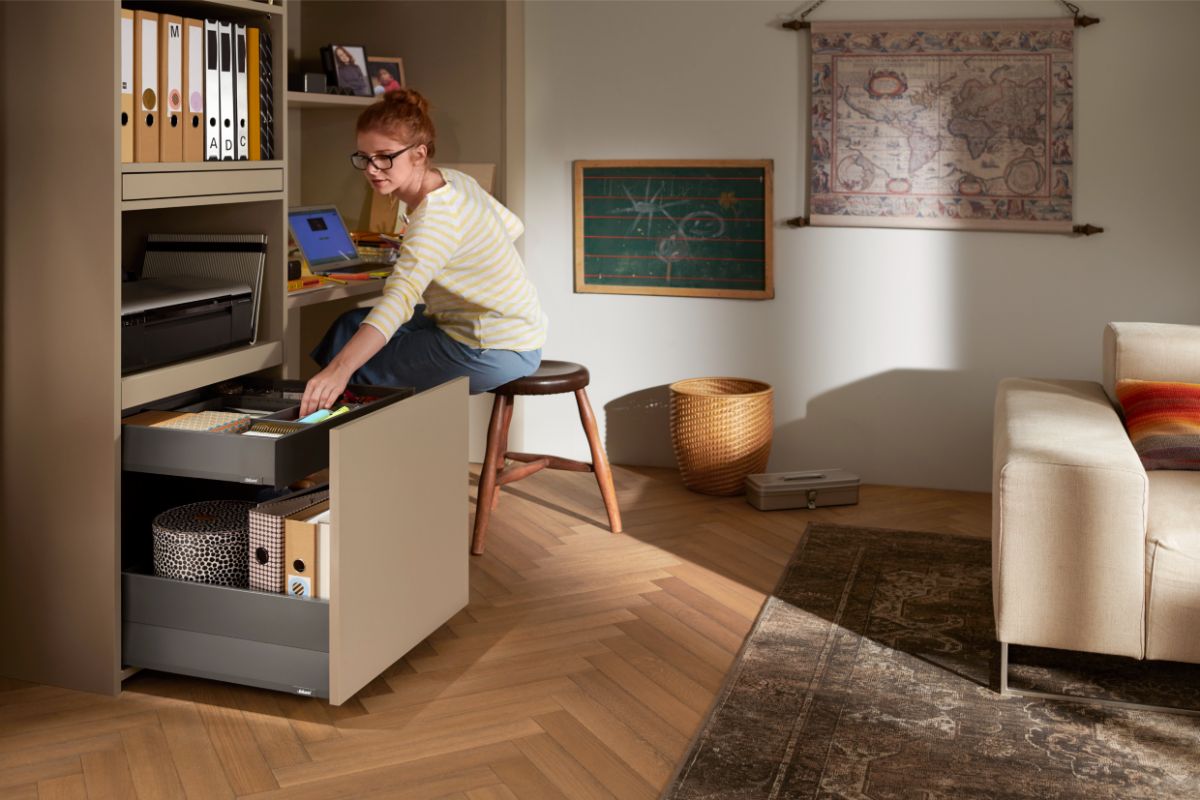 Béžová pracovná zostava s hlbokými sivými zásuvkami na zakladače a kancelárske potreby v modernom interiéri.