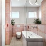 Kúpeľňa s bielym umývadlom na skrinke, ružovým obkladom veľkým zrkadlom a toaletou.