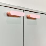 Detail ružových úchytiek, tlačených na 3D tlačiarni, na sivej dvojdverovej skrinke.