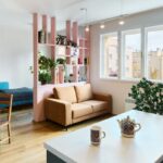 Ružová deliaca stena s kvetmi nad hnedou pohovkou, drevený jedálenský stôl v pozadí a biela kuchynská doska v popredí.