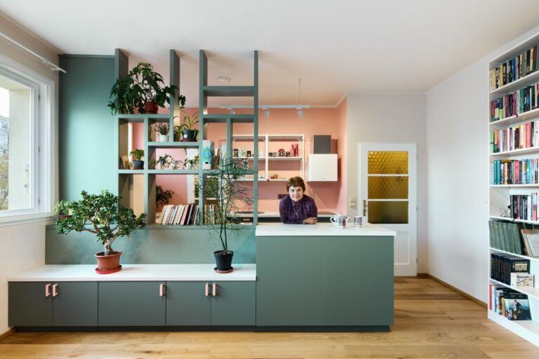 Žena opierajúca sa o tmavozelený kuchynský ostrov vedľa policovej steny.