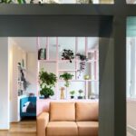 Pohľad cez policovú zostavu na ružovú policu a svetlohnedú pohovku pod ňou.