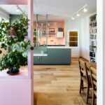 Byt s drevenou podlahou, tmavozelenou skrinkou s kuchynským ostrovčekom a ružovou policou v popredí.