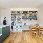 Vysoká biela knižnica vedľa šedého príborníka a drevený jedálenský stôl na drevenej podlahe.