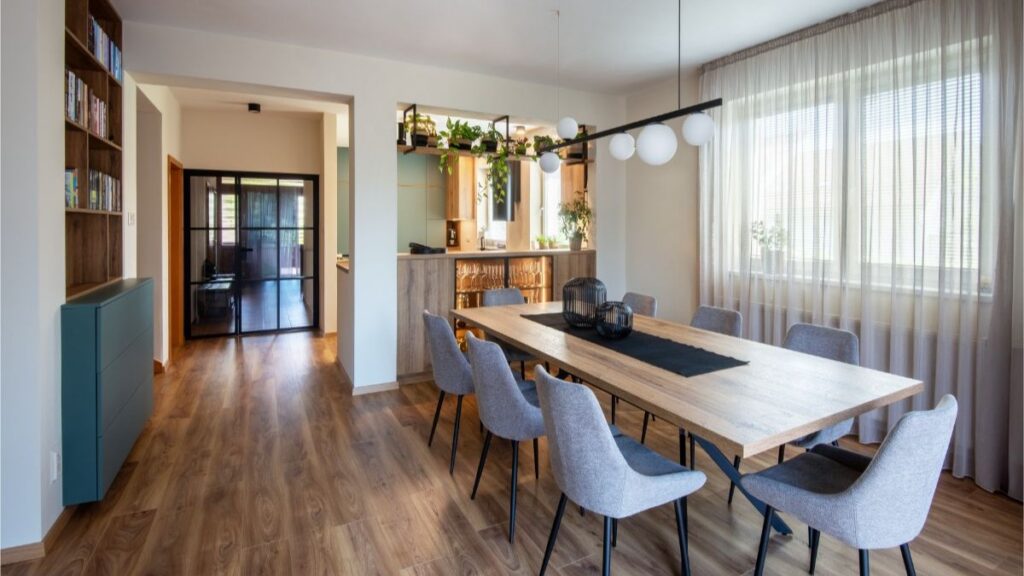 Moderný drevený jedálenský stôl, sivé čalúnené stoličky a dizajnové guľové svietidlo v otvorenom svetlom interiéri.