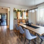 Moderný drevený jedálenský stôl, sivé čalúnené stoličky a dizajnové guľové svietidlo v otvorenom svetlom interiéri.