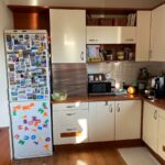 Krémová kuchynská linka s tmavou pracovnou doskou a biela chladnička pokrytá farebnými magnetkami pred renováciou.