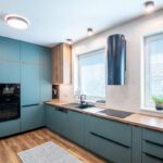 Matná petrolejová kuchynská linka s drevenou pracovnou doskou a čierny valcový digestor na bielej obkladačke.