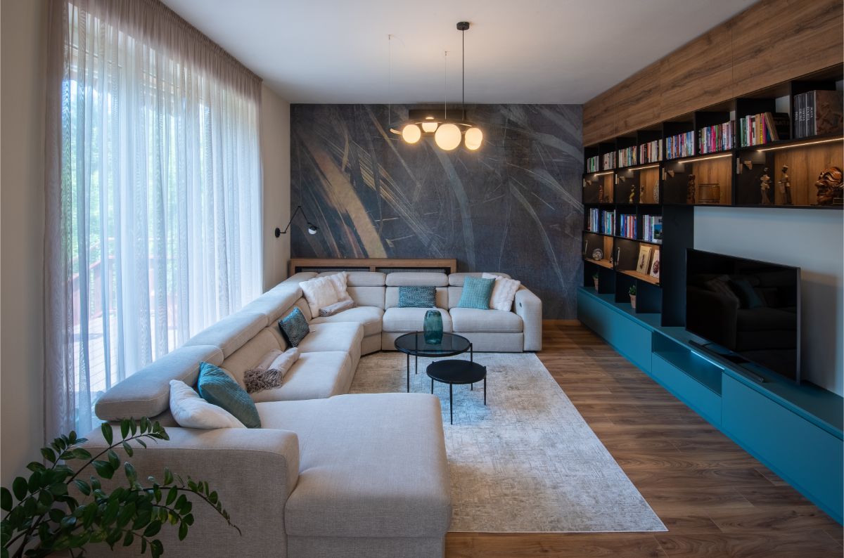 Sivá rohová sedačka, modrá obývacia stena a tmavá umelecká tapeta v modernom mestskom byte.