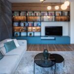 Elegantná modrá TV zostava s drevenými policami, okrúhly sklenený konferenčný stolík a čierne kruhové svietidlo.