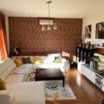 Pôvodná obývacia izba s tehlovou stenou, bielou rohovou sedačkou a tmavým konferenčným stolíkom pred renováciou.