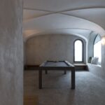 Miestnosť s biliardovým stolom pod nízkou klenbou, sivou omietkou, oblúkovým oknom a liatou kamienkovou podlahou.