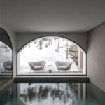 Vnútorný bazén s veľkým oblúkovým oknom s výhľadom na zasnežený exteriér a dve kreslá.