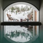 Vnútorný bazén s veľkým oblúkovým oknom s výhľadom na zasnežený exteriér a dve kreslá.