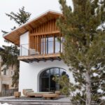 Vila s exteriérom alpských chát a bielou fasádou, dreveným obkladom. a terasou s posedením.