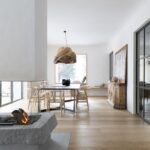 Otvorený interiér s dubovou podlahou, moderným visiacim svietidlom, čiernym stolom a masívnou drevenou komodou pri krbe.