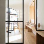 Svetlá chodba s drevenou lavicou, čiernym kovovým presklením a dreveným výklenkom na sedenie pri bielom okne.