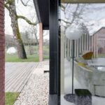 Pohľad do interiéru domu cez veľkoformátové presklenie v čiernom ráme.