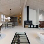 Otvorený obytný priestor s čiernymi krbovými kachľami, dreveným stropom a koženým kreslom pri sklenenom vstupe do vinotéky.