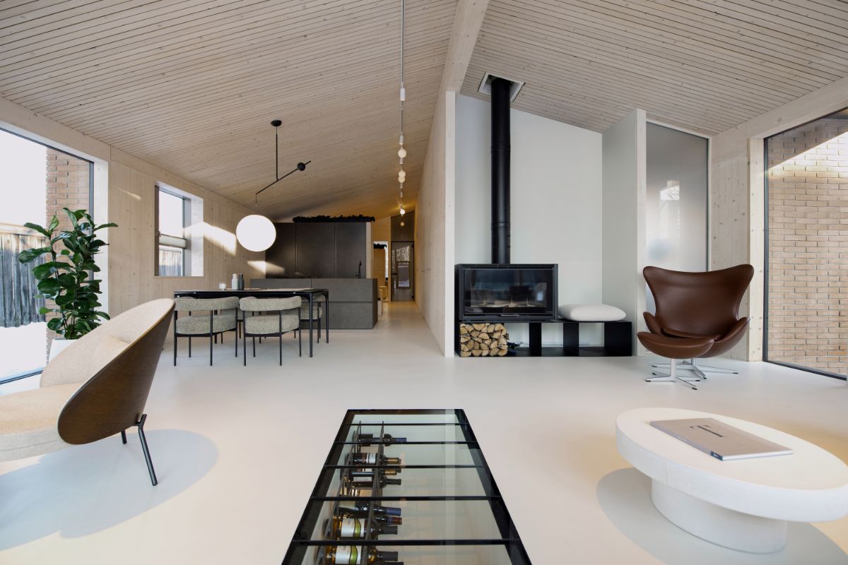 Otvorený obytný priestor s čiernymi krbovými kachľami, dreveným stropom a koženým kreslom pri sklenenom vstupe do vinotéky.