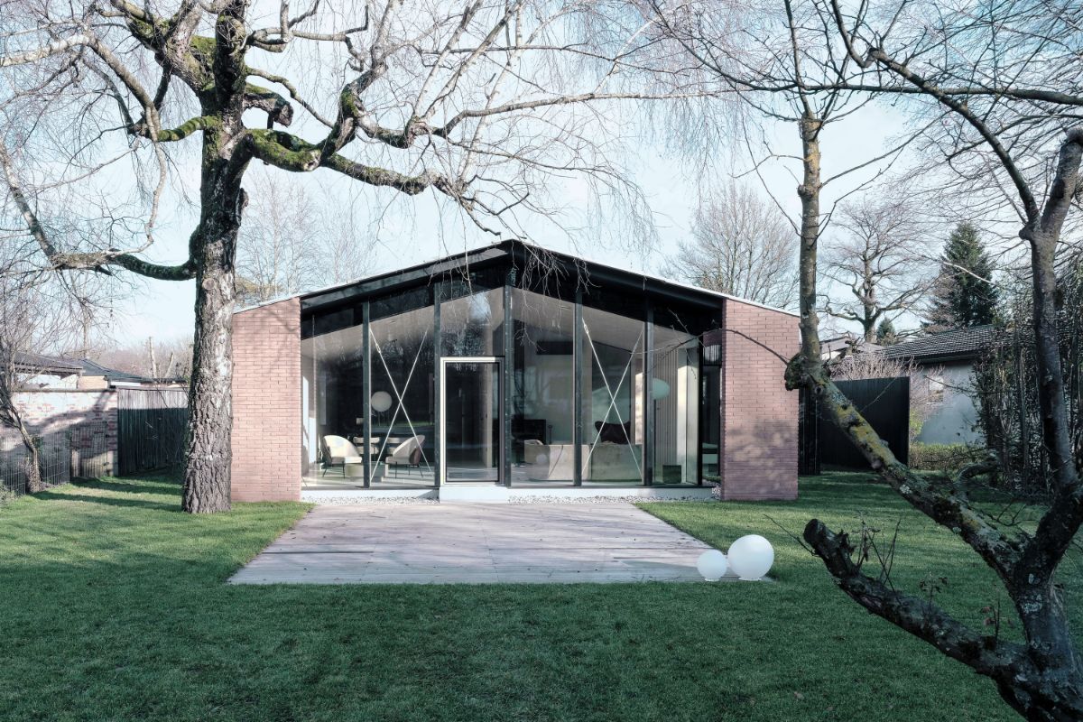Zmodernizovaný dom s presklenou fasádou s čiernym rámom, červeným tehlovým obkladom a svetlou kamennou terasou.