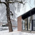 Časť zrekonštruovaného domu s tehlovým stĺpom a veľkoformátovým presklením v čiernom ráme.