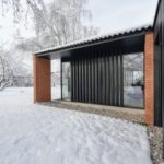 Krytá terasa s čiernym podhľadom, vertikálnym lamelovým tienením a červeným tehlovým stĺpom.