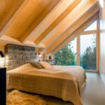 Podkrovná spálňa s dreveným obložením, atypickým šikmým presklením a sklenenými dverami.