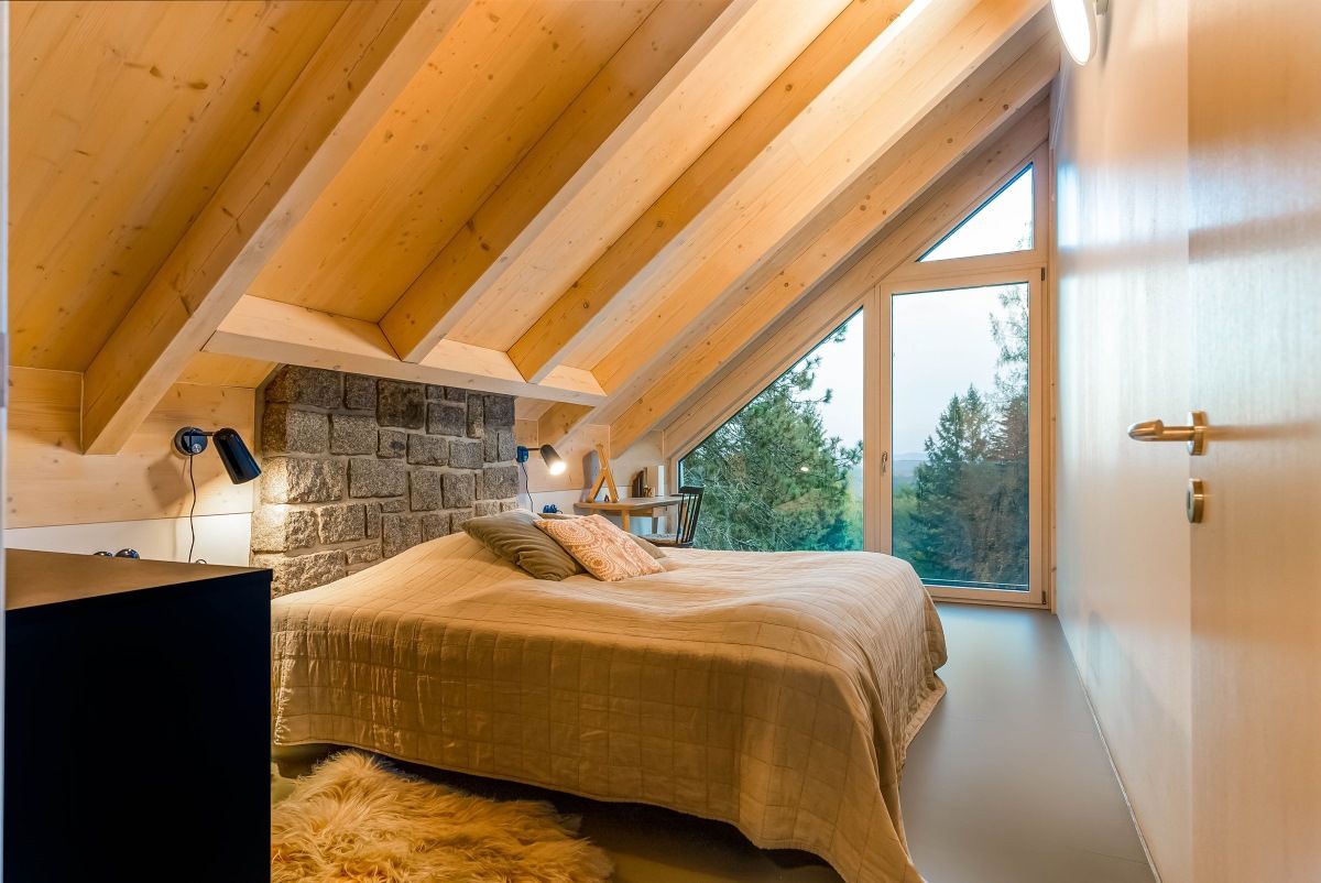 Podkrovná spálňa s dreveným obložením, atypickým šikmým presklením a sklenenými dverami.