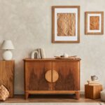 Drevená komoda s polkruhovými úchytkami, béžová stierka na stene, ratanový kôš a minimalistické obrazy v drevenom ráme.