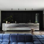 Kuchyňa s antikorovým ostrovom s drezom a zásuvkami pred zostavou skriniek s drevenými panelmi.