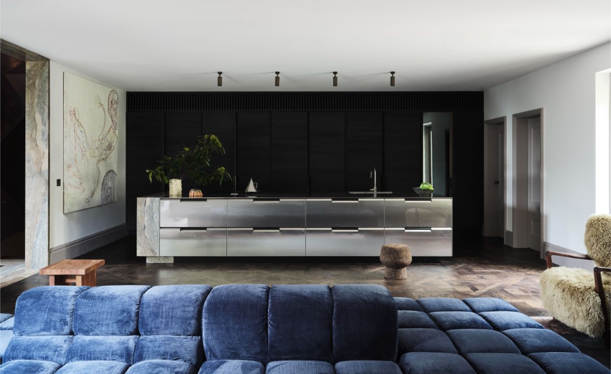 Kuchyňa s antikorovým ostrovom s drezom a zásuvkami pred zostavou skriniek s drevenými panelmi.