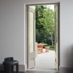 Pohľad cez otvorené dvojkrídlové dvere na dláždenú terasu so záhradným nábytkom.